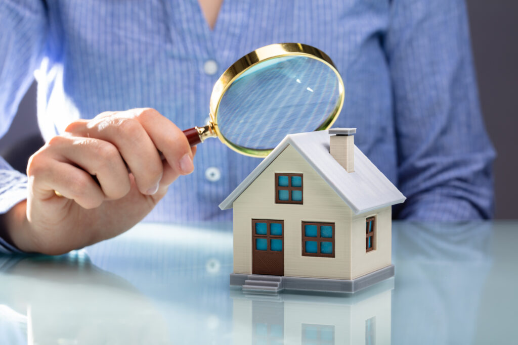 Person looking at a little house model with a magnifying glass
